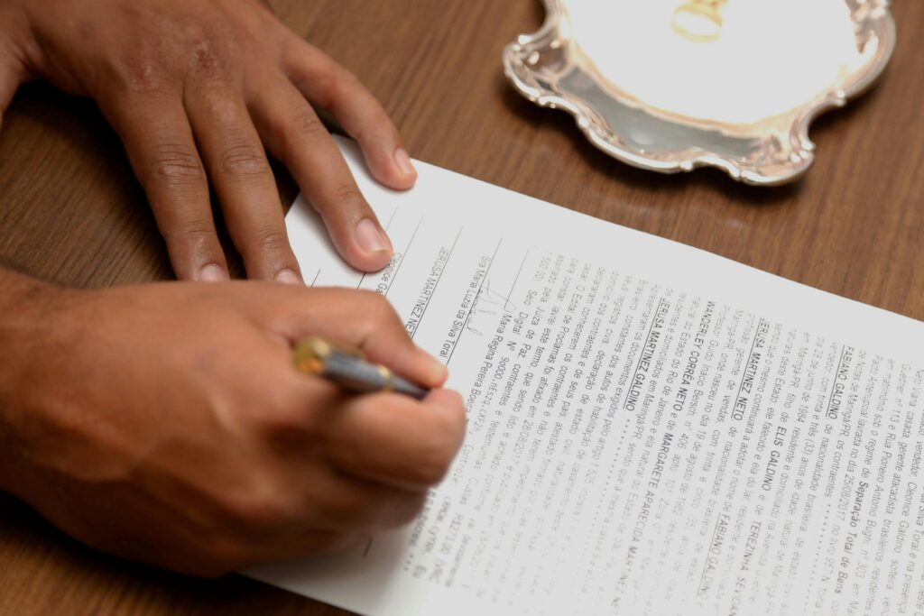 Hand signing a contract on a wooden desk, emphasizing business formalities.